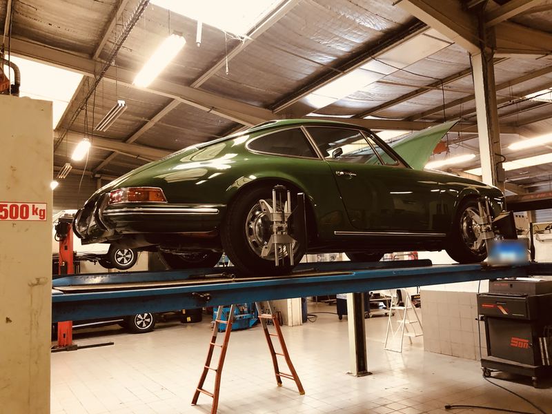 Porsche 911 ancienne verte levée sur un pont élévateur de l'atelier, capteurs fixés sur les roues