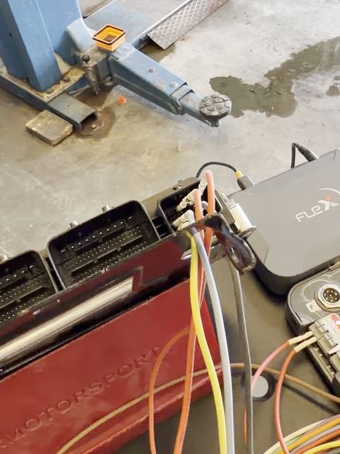 Calculateur posé sur un support de banc Magicmotorsport et câblé à l'outil FLEX, pont élévateur en arrière-plan