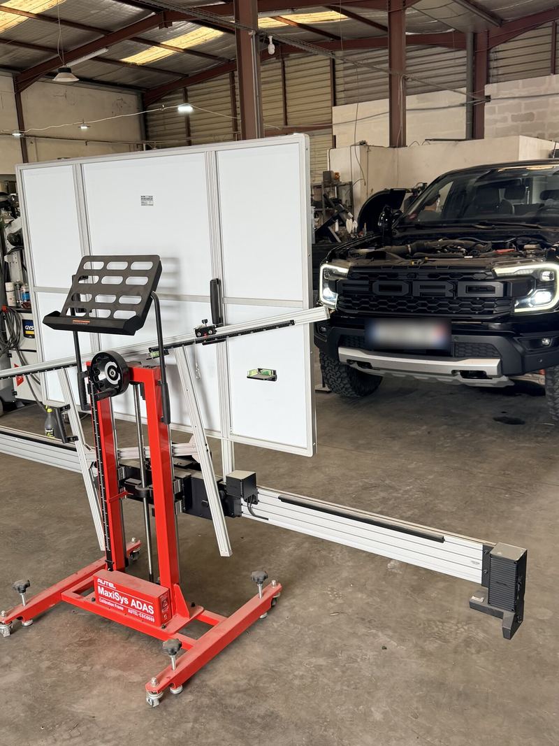 Portique de calibrage Autel MaxiSys ADAS (cadre rouge) devant un pick-up Ford à l'atelier, plaque floutée